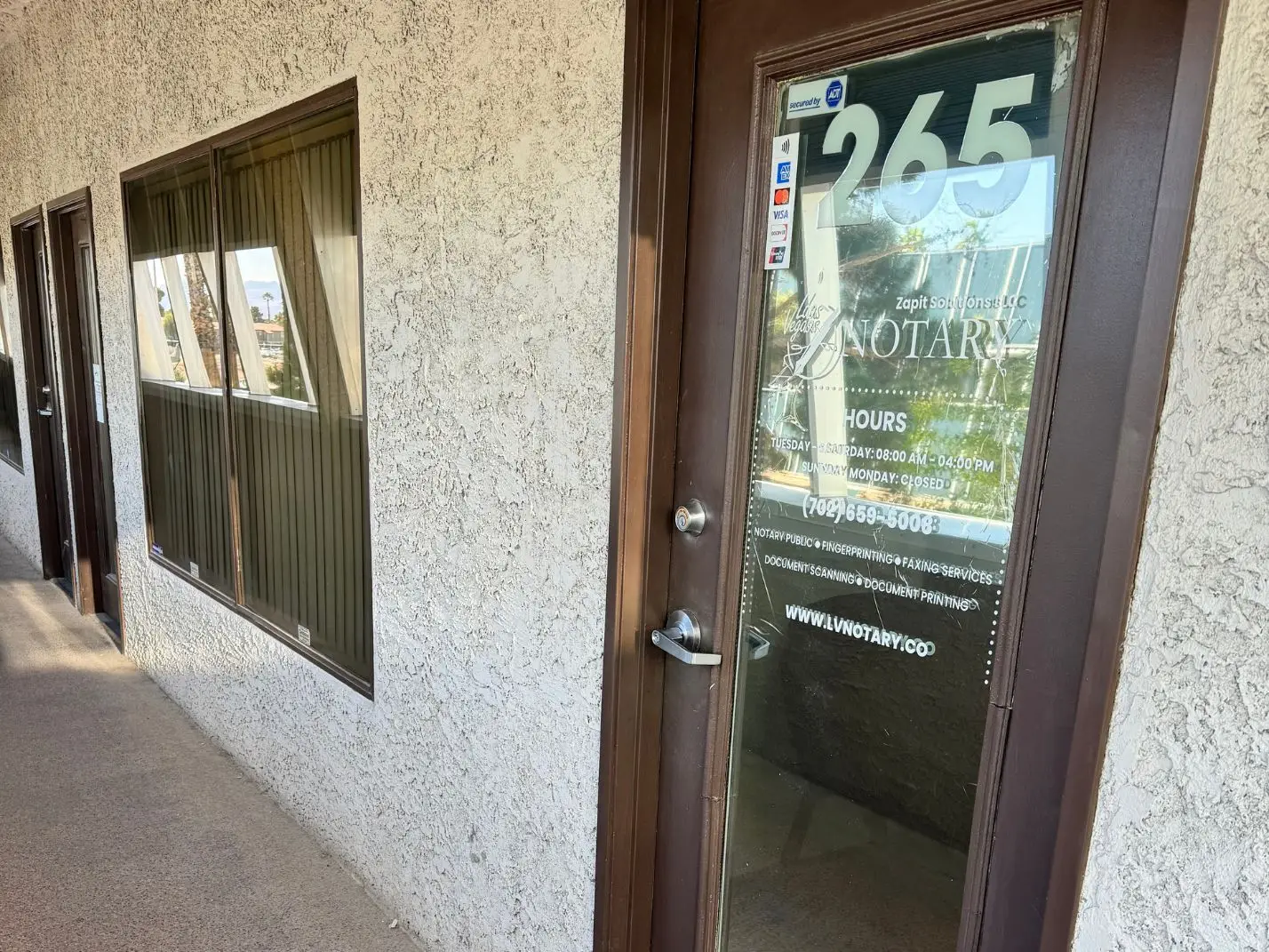 Entrance to Las Vegas Notary office featuring a brown door with glass displaying business hours, services offered, and contact information.